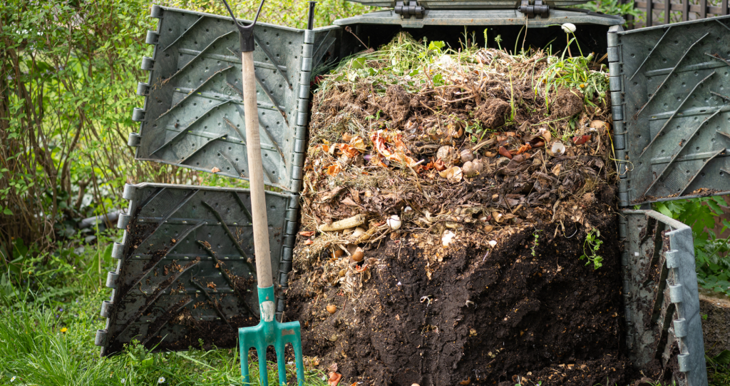 Opening the doors to a compost bin for rotation. A pitchfork is nearby as a great tool to rotate green and brown materials.