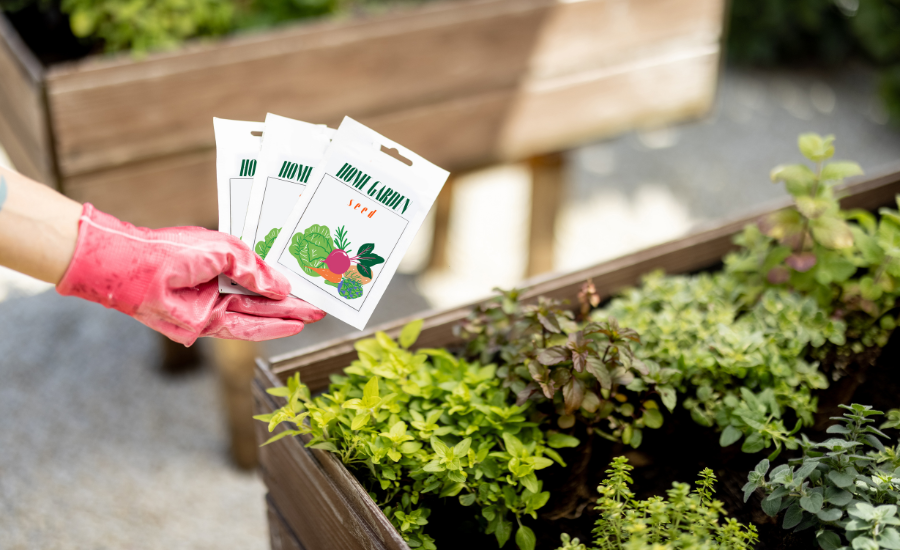 A gardener's hand is holding home-made seed packages near their container gardens.